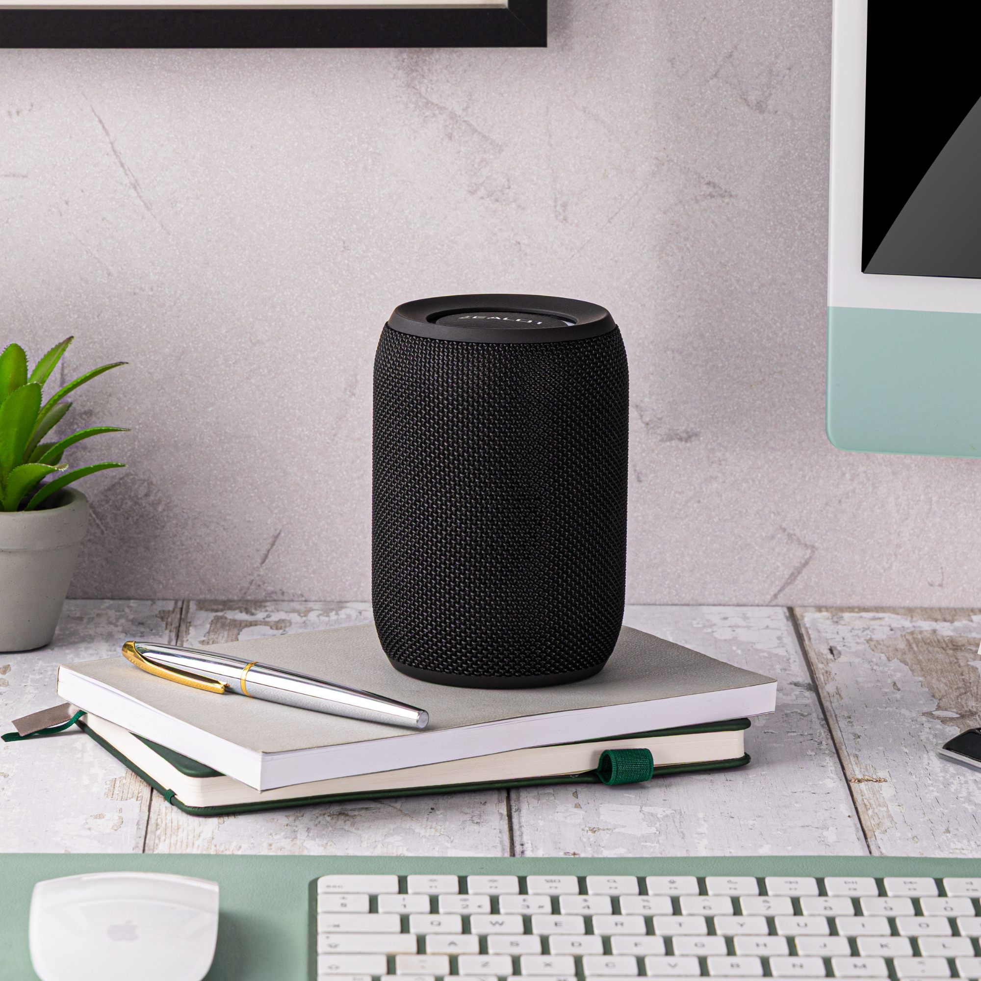 Black smart speaker on a notebook with a plant and pen in the background